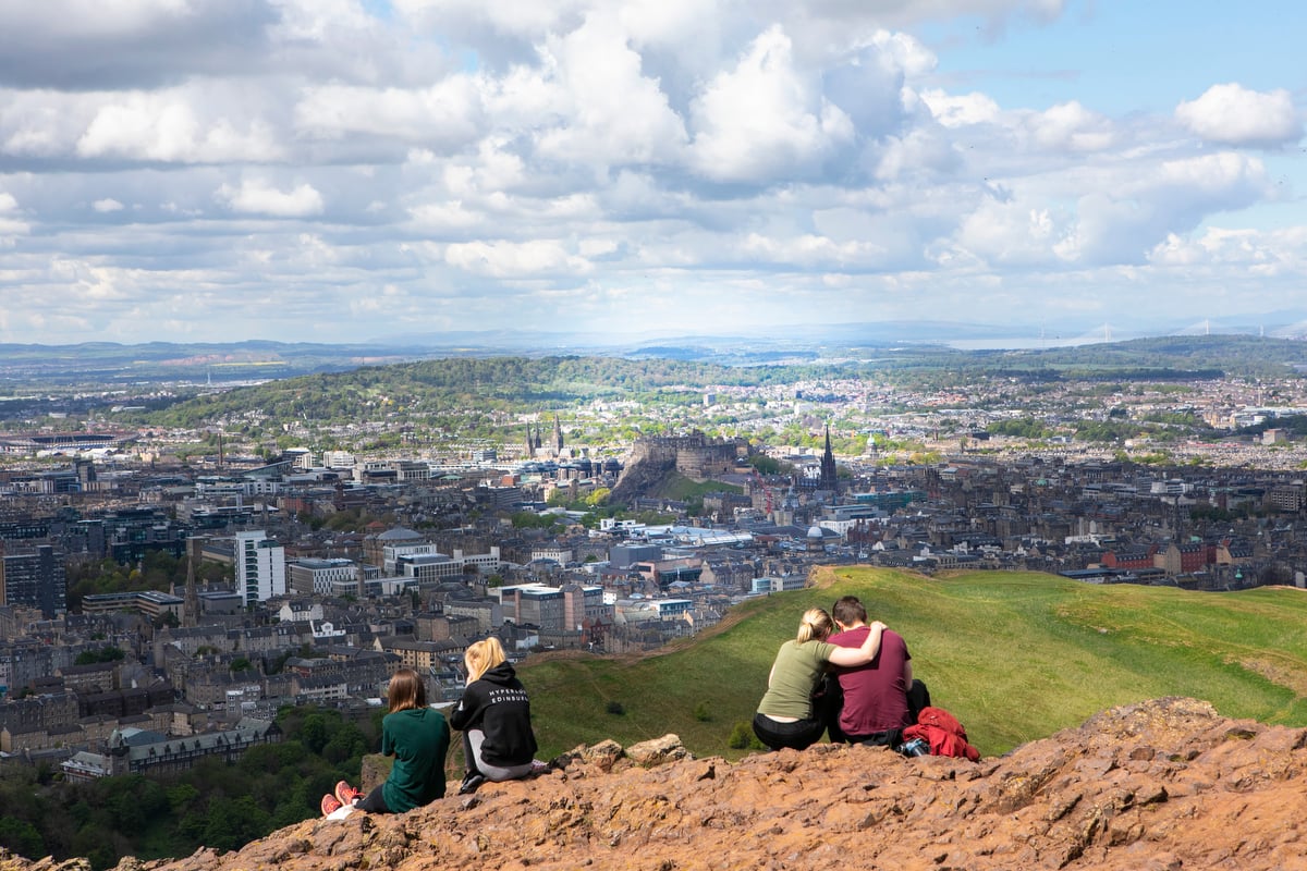 Couple sat on Arthur Seat looking out towards Edinburgh city below