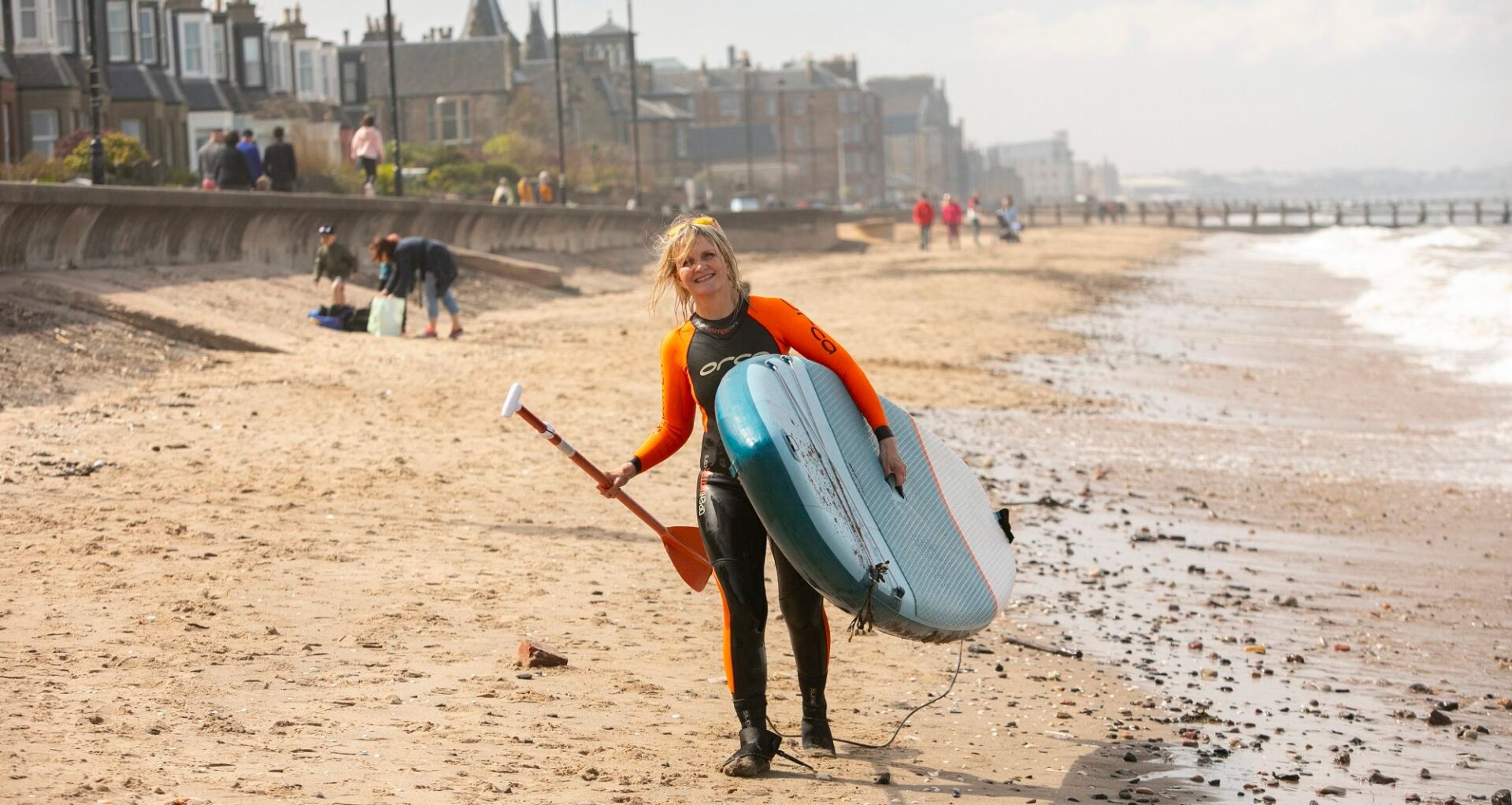 Portobello lady carrying Waterboard walking along sand