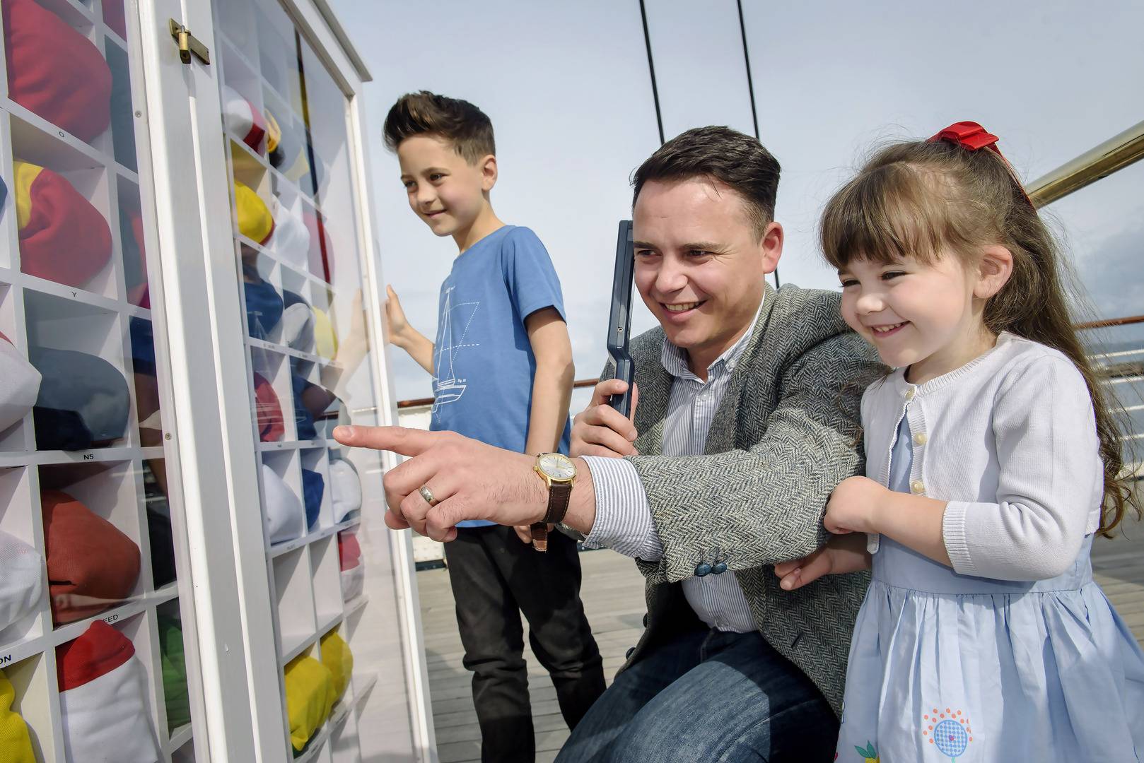 Father, son and daughter look at the signal flags which are organised into a cabinet., Helen Pugh