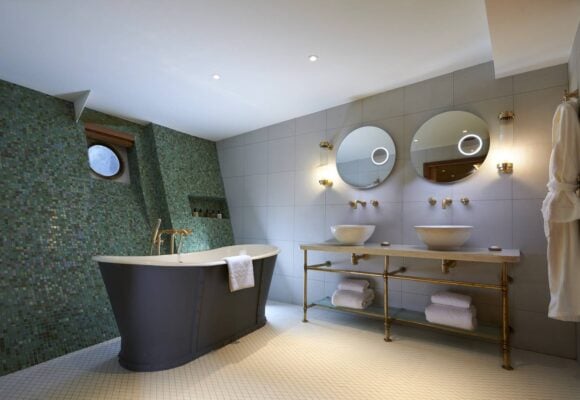A large bathroom with free-standing roll-top bath, Jack & Jill wash basins and a green mosaic sloping wall. , Jeremy Rata