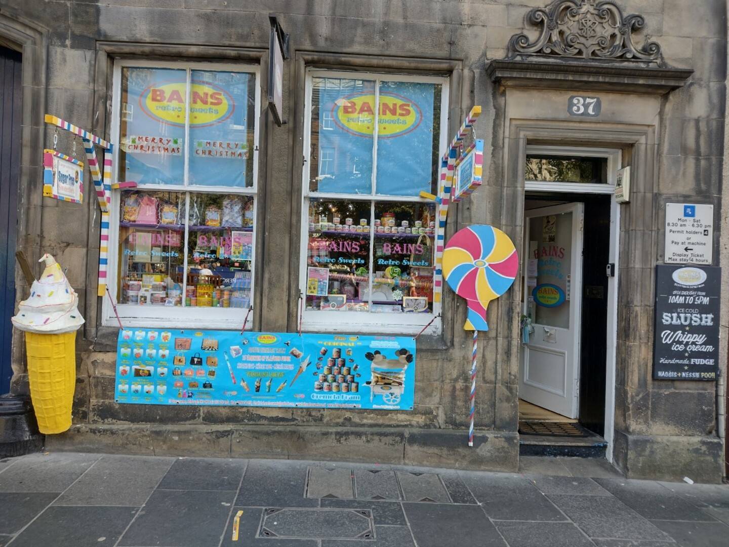 Store front featuring jars of old fashioned sweets in the window, giant lollipop and ice cream standing outside