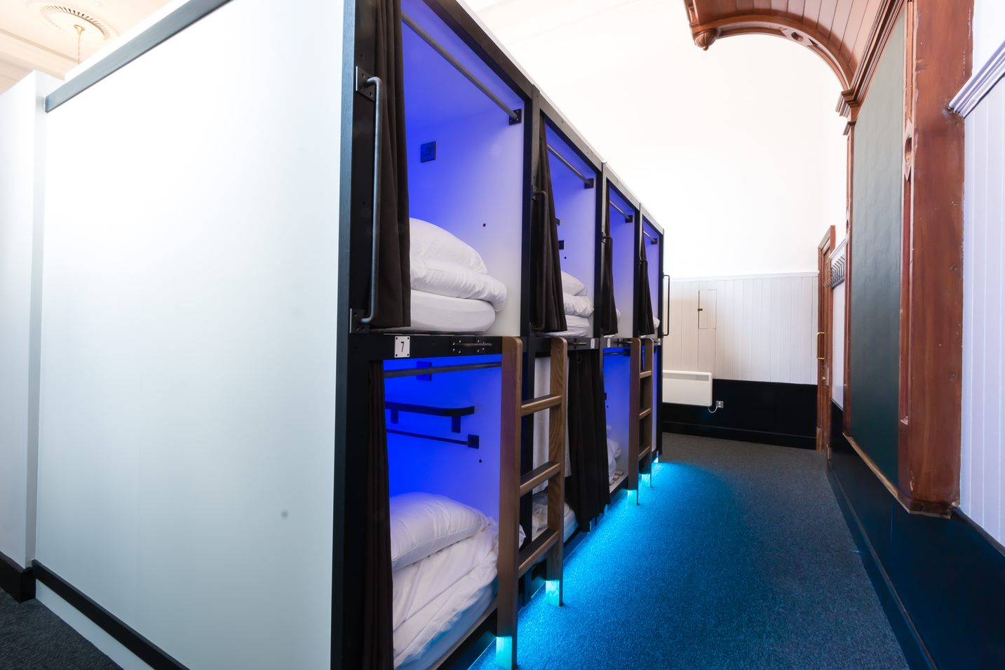 view of 8 sleeping pods in the courtroom. All with linen and ambient light., code Hostels