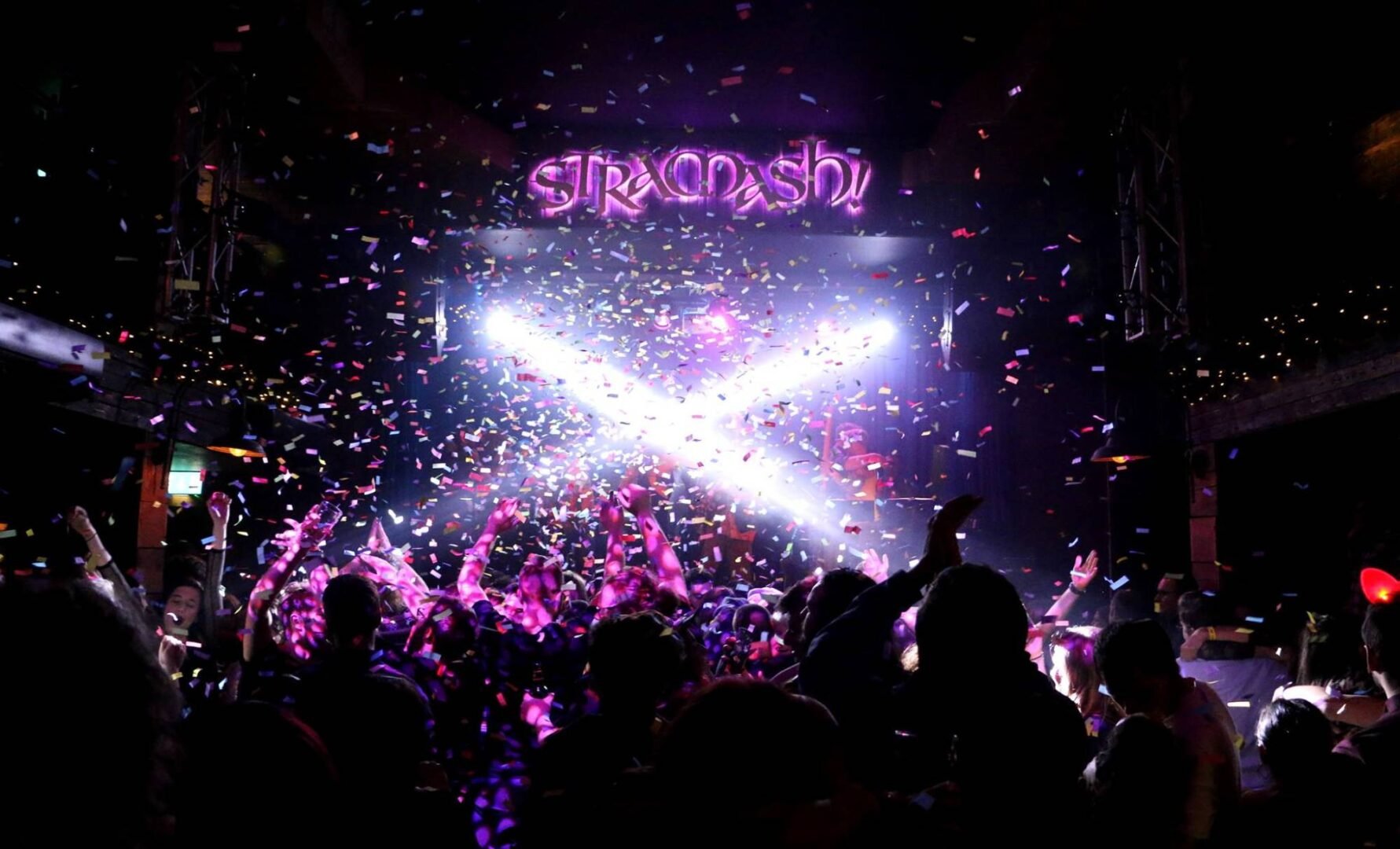 Stramash stage lit with white cross lights.  Confetti falling and crowd hands in air., Stramash