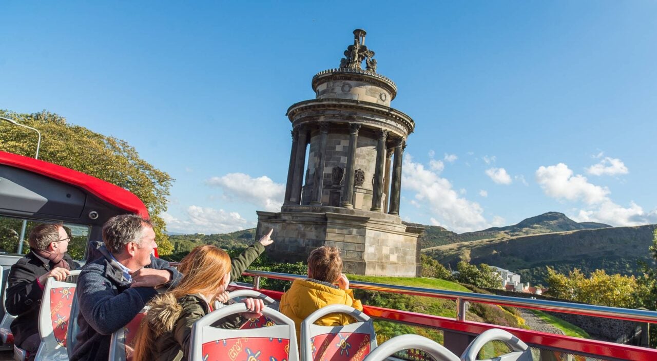 Image of open top bus with visitors looking at the Burns Monument on a sunny day,© Edinburgh Bus Tours