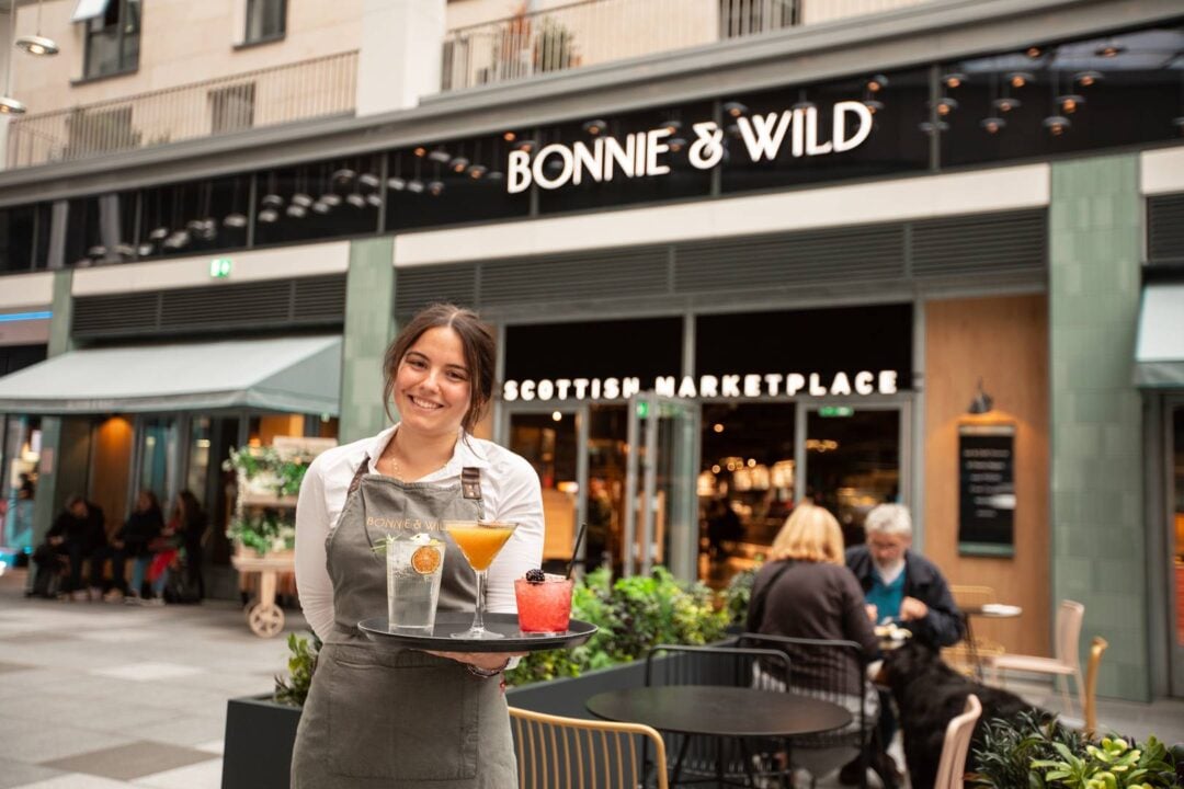 Image of smiling waitress with tray of drinks  in front of Bonnie & Wild in the St James Quarter