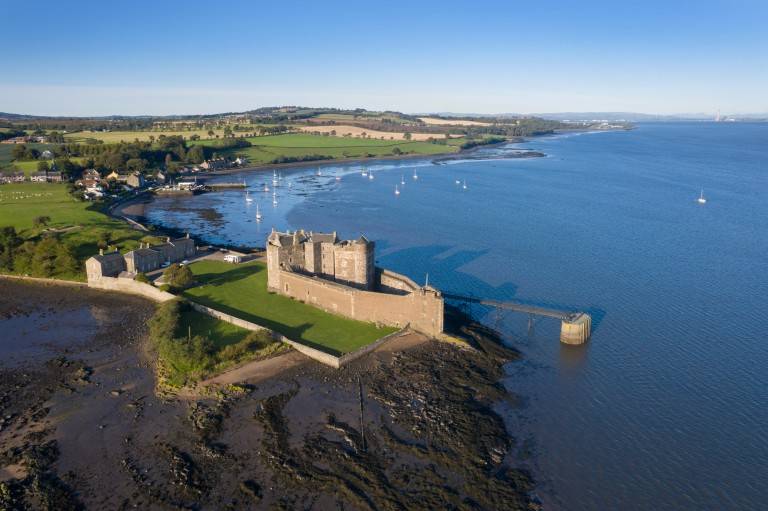 Aerial image of a castle on the banks of the Forth on a sunny day.