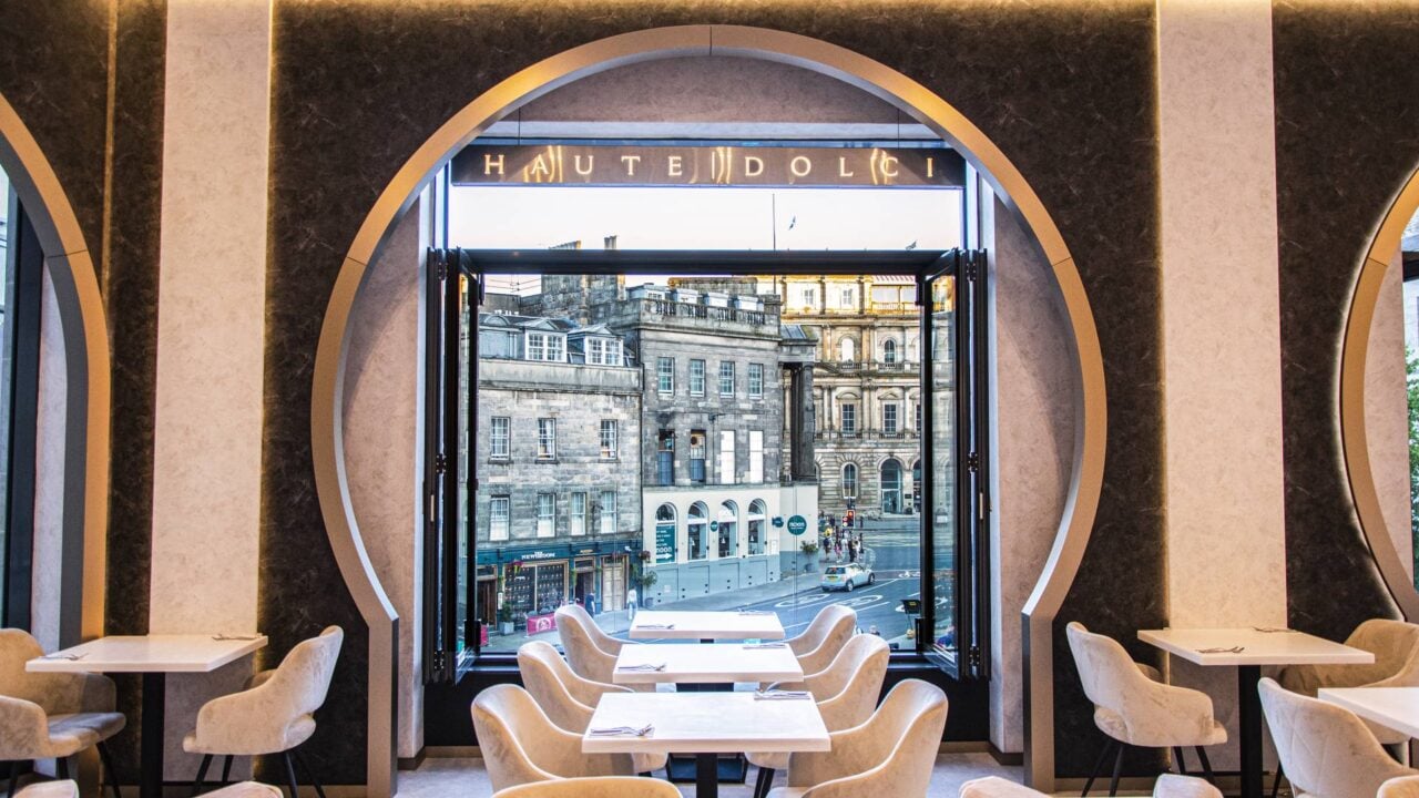 The image shows the inside of Haute Dolci's restaurant with pink chairs and white tables and a view of St James Square through the window. Above the window is Haute Dolci's signage.,© Haute Dolci