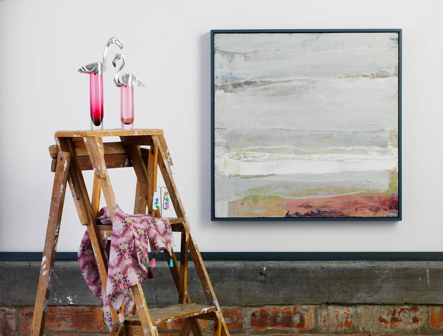 Image with abstract painting hung on white wall beside step ladders with pink glasses