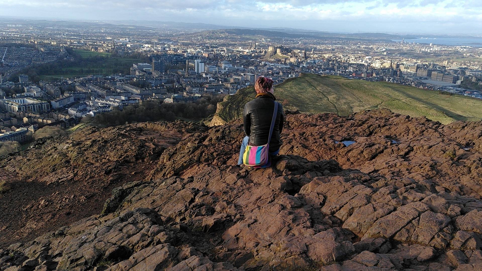 Person sitting at the summit of Arthur's Seat enjoying the view, Angus Miller, Geowalks