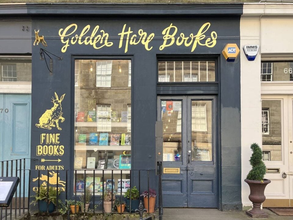 Dark blue shop front with beautiful golden lettering that spells Golden Hare Books. Large window with four rows of books displayed.,© Golden Hare Books 2023
