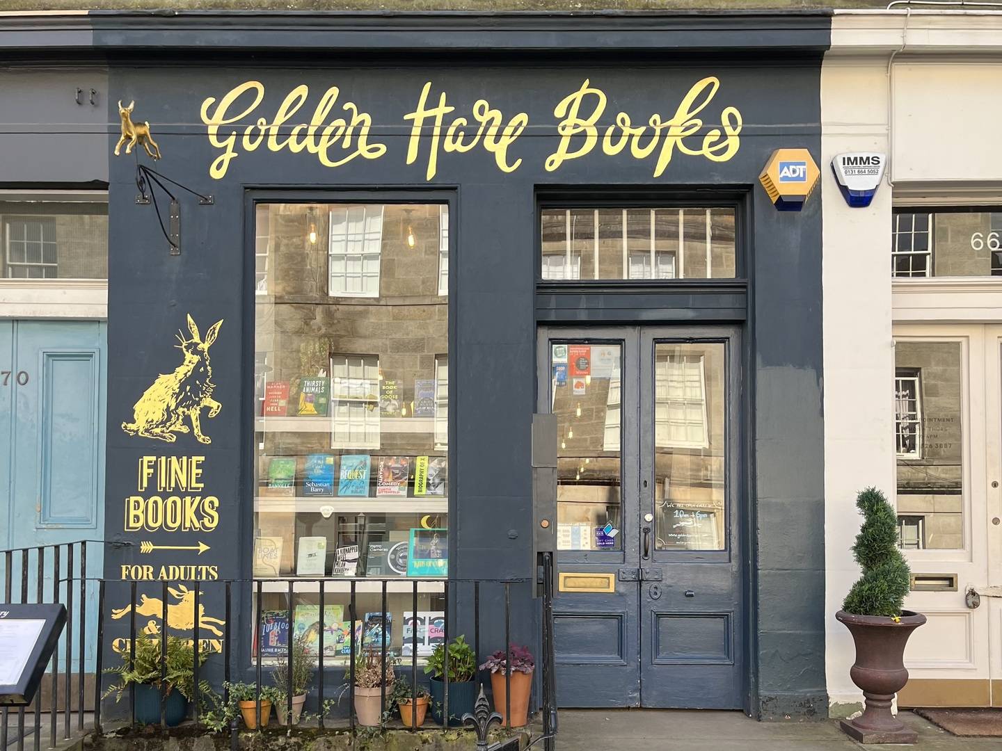 Dark blue shop front with beautiful golden lettering that spells Golden Hare Books. Large window with four rows of books displayed.,© Golden Hare Books 2023