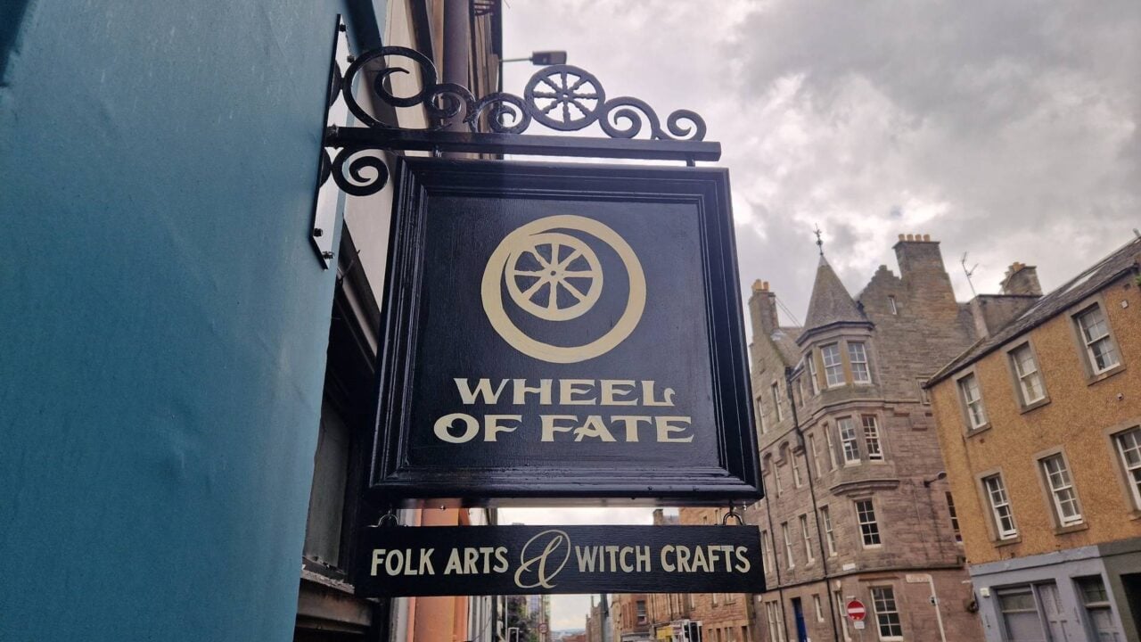 Black sign with yellow writing saying wheel of fate folk arts and witch crafts