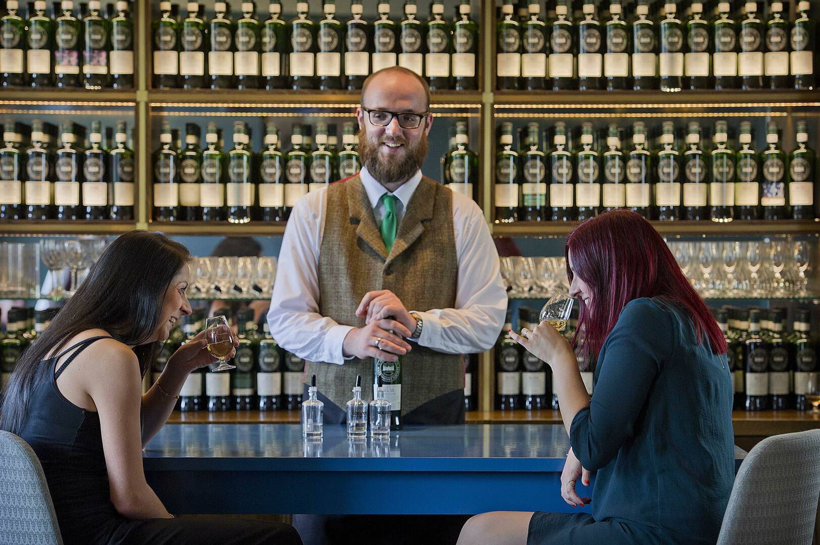 Bar tender serving two female customers whisky samples in tasting bar.,© Eat Walk Tours Limited