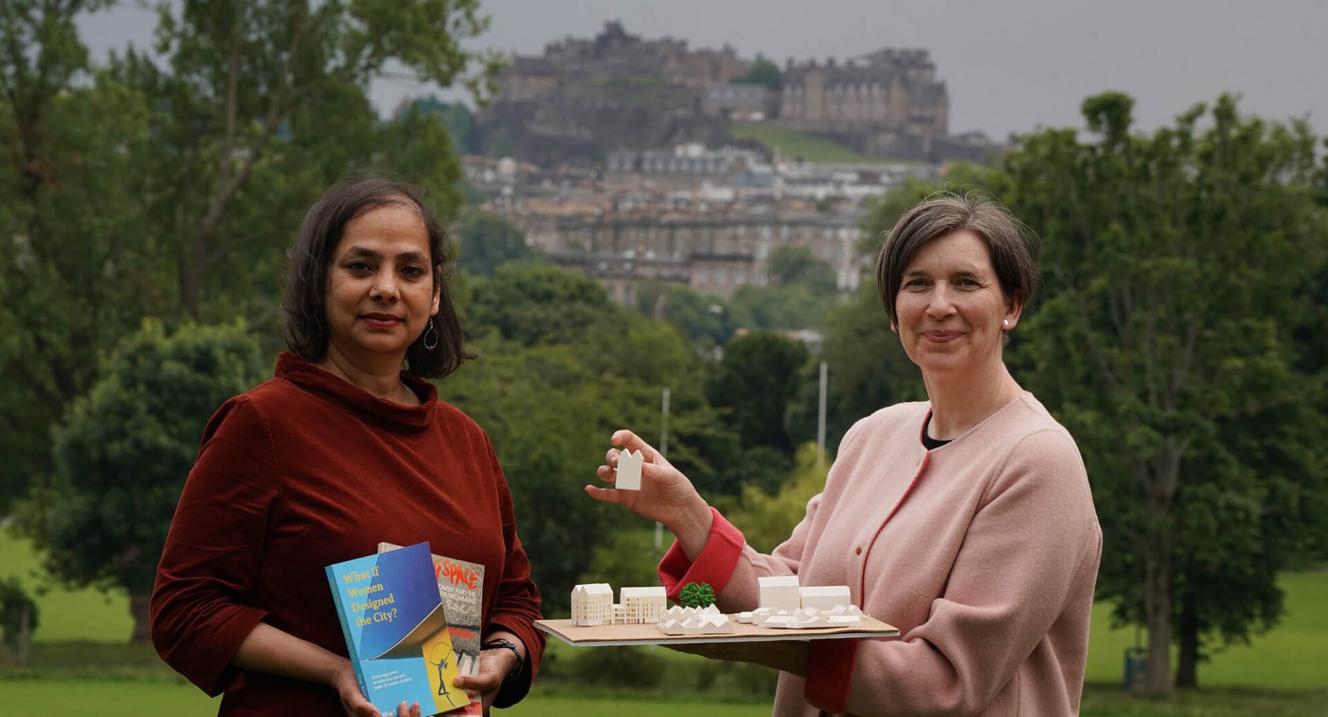 2 females standing in grassy area with Edinburgh Castle in background.