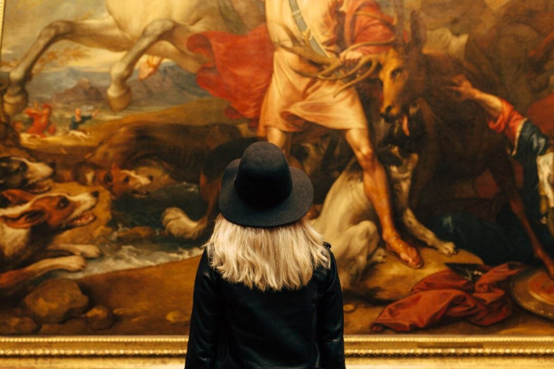 A woman in a hat looking at a large painting,© National Galleries of Scotland