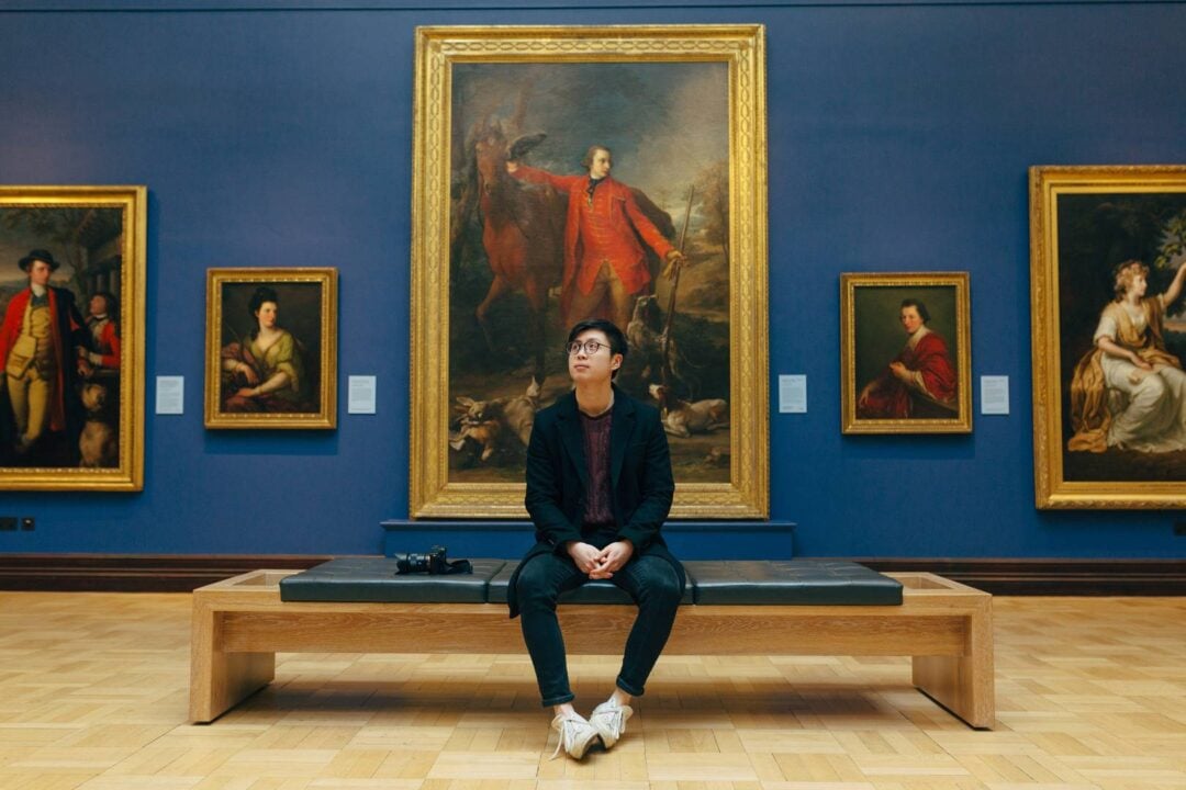 A man sitting in a gallery full of portraits,© National Galleries of Scotland