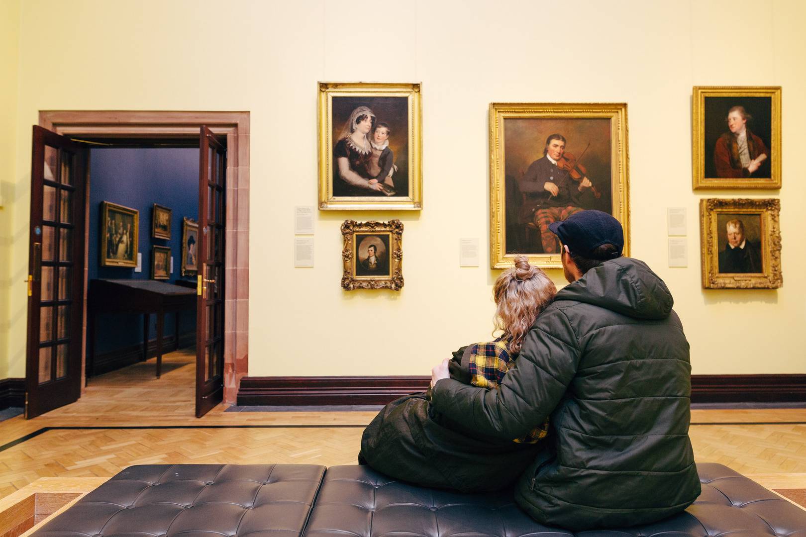 A couple hug while looking at a room full of portraits in a gallery, National Galleries of Scotland