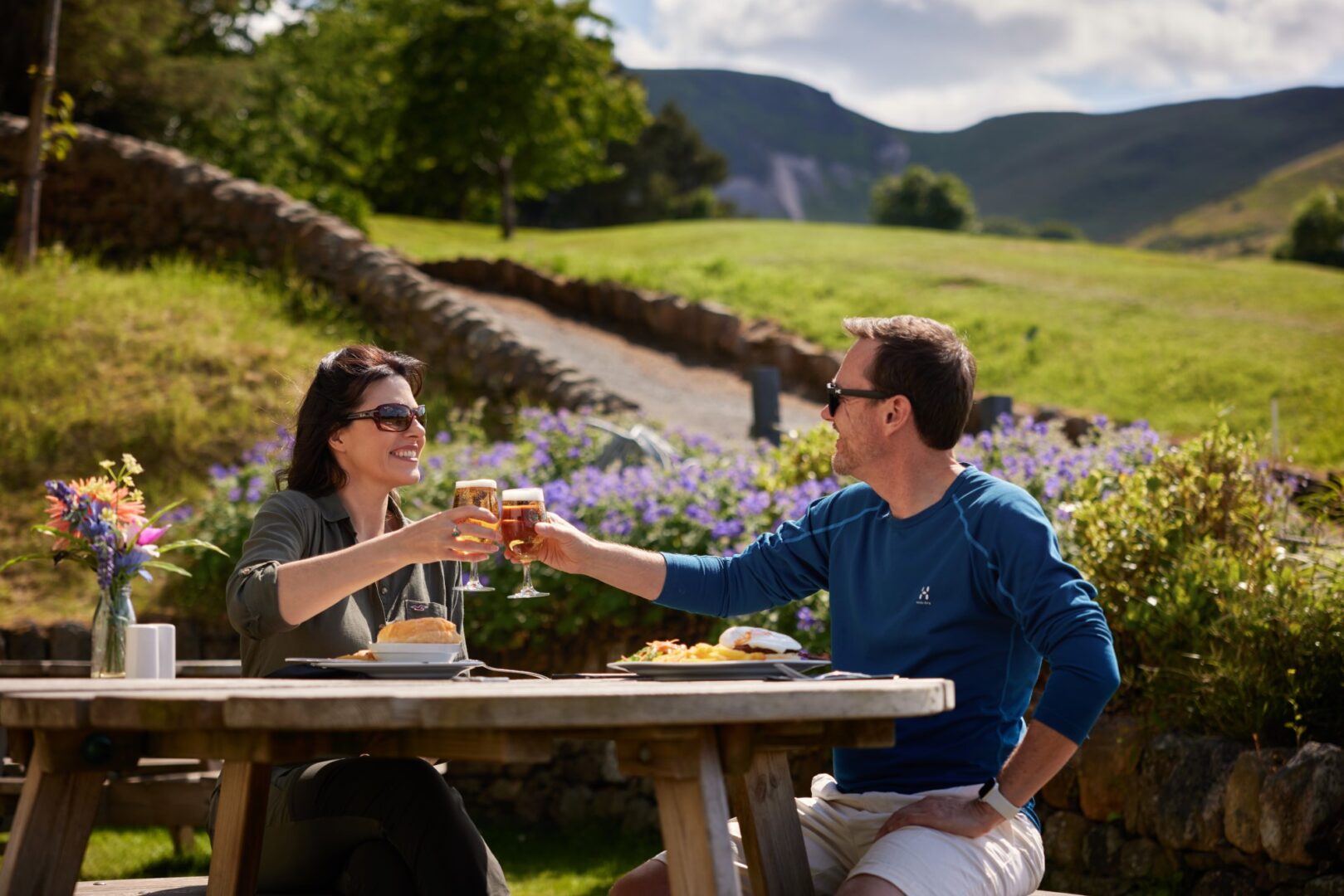 Couple having lunch and cheers their glasses with The Pentland Hills in the background.
