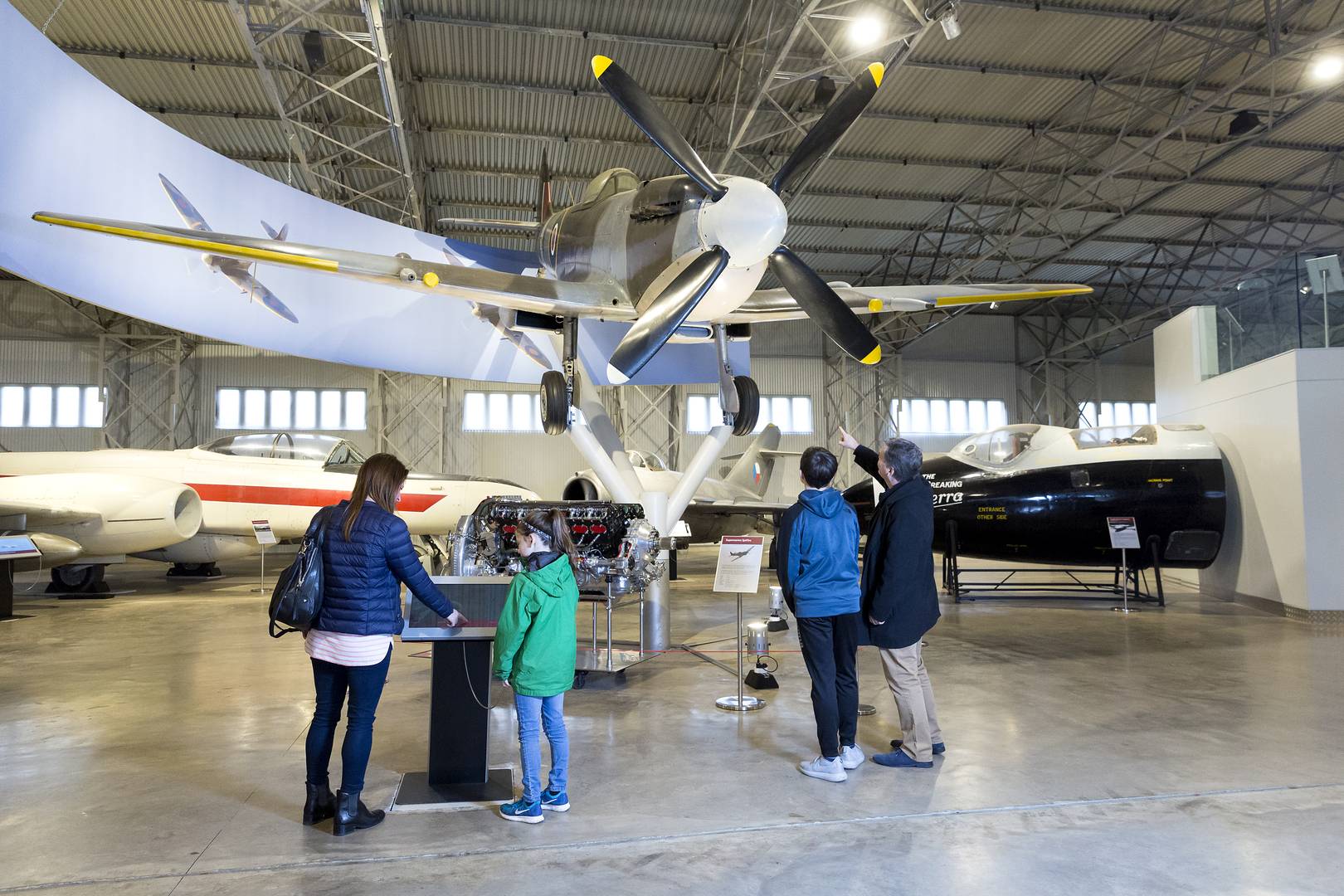 A family underneath a Spitfire aircraft in the Military Aviation Hangar at the National A Museum of Flight © Ruth Armstrong Photography, Image © Ruth Armstrong Photography