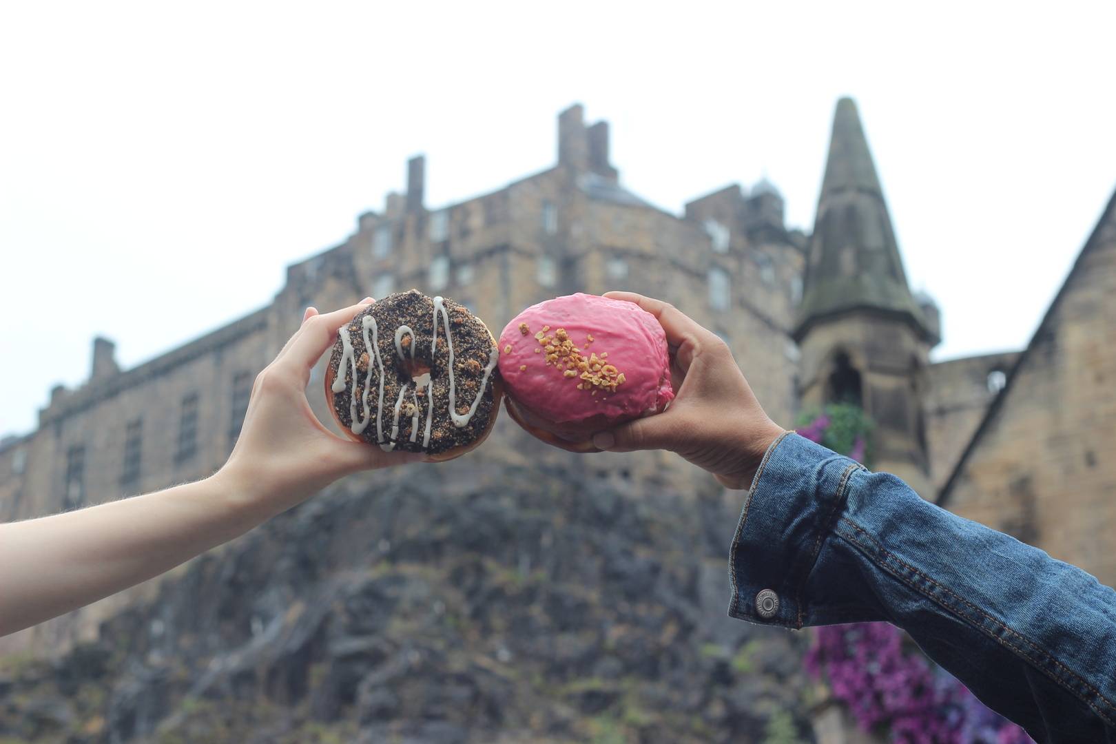 Hands holding out donuts in front of Edinburgh castle