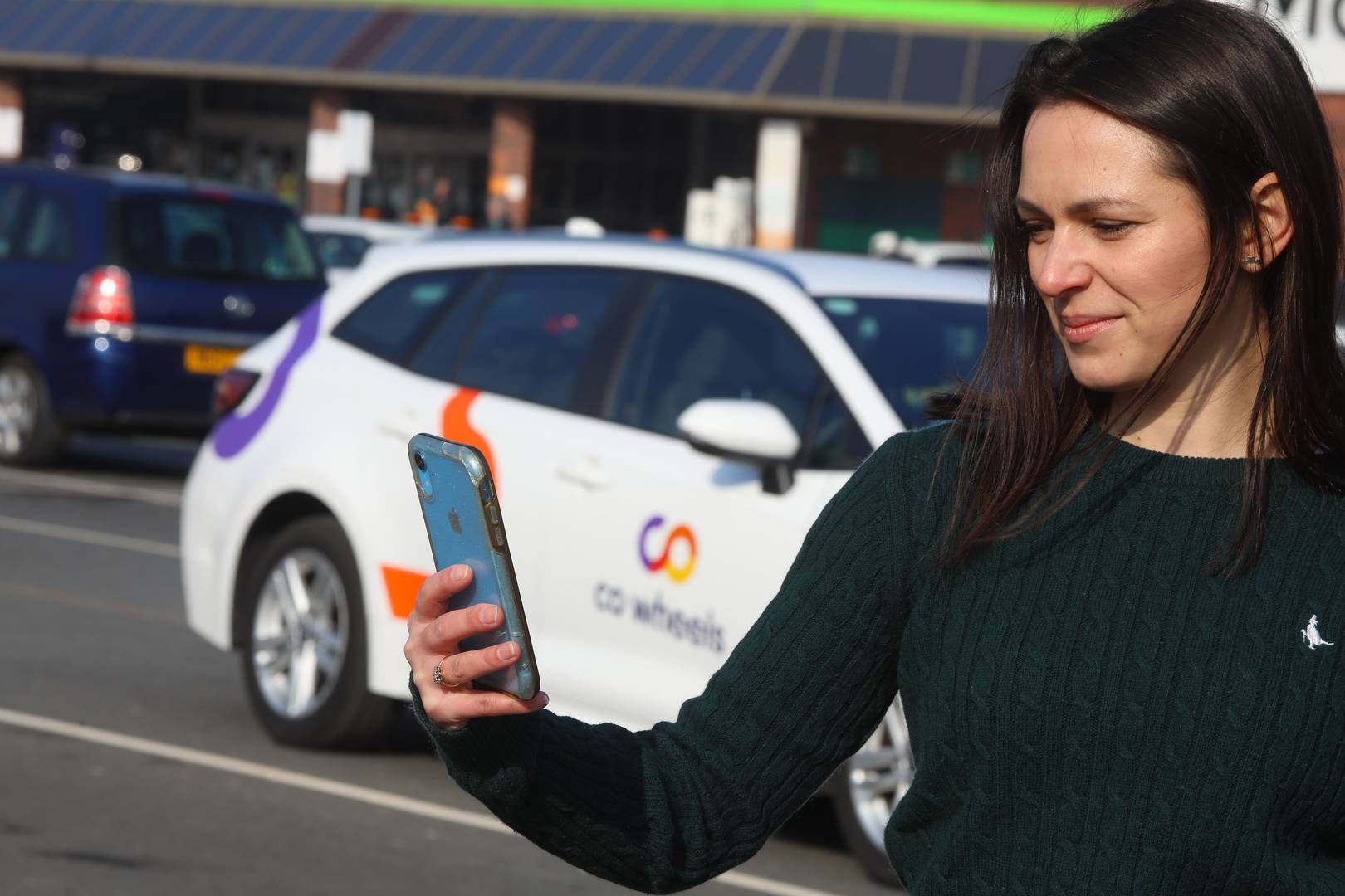 Woman on her phone in front of Co Wheels car