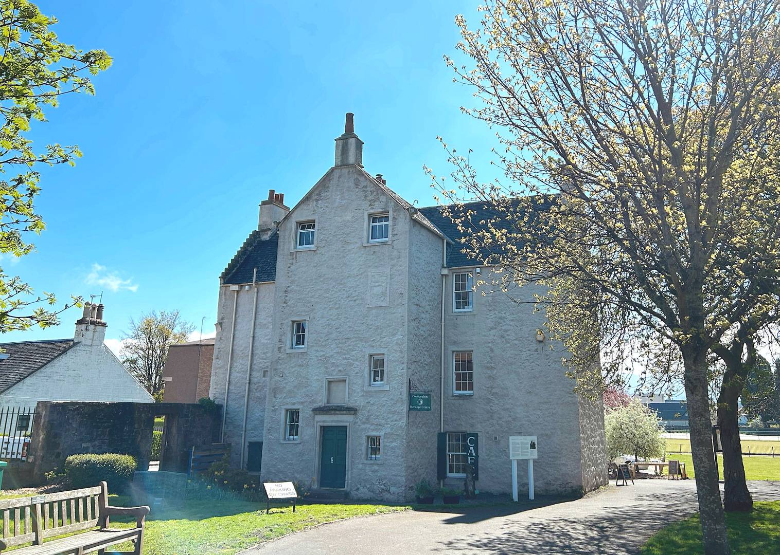 An image of a lime-washed building. It has gable ends at either side. The sky is clear blue and two trees frame the image.