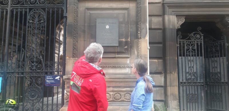 Tour guide showing woman plaque on Edinburgh University's Medical School building