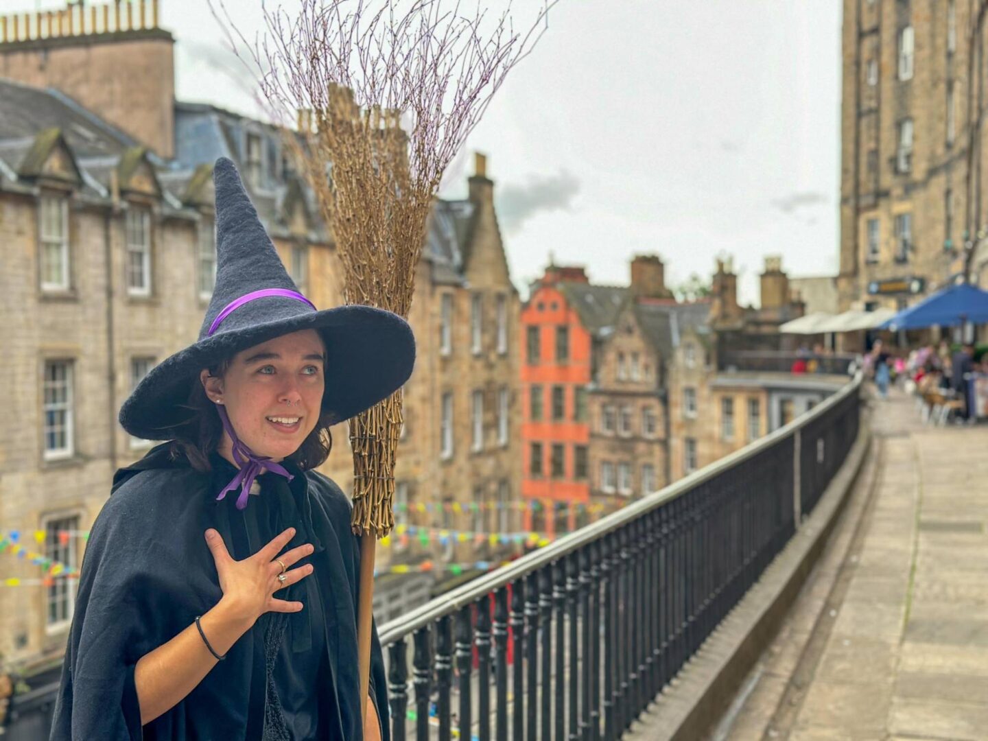 Witch guide with black pointy hat and broom stick talking in Edinburgh old town