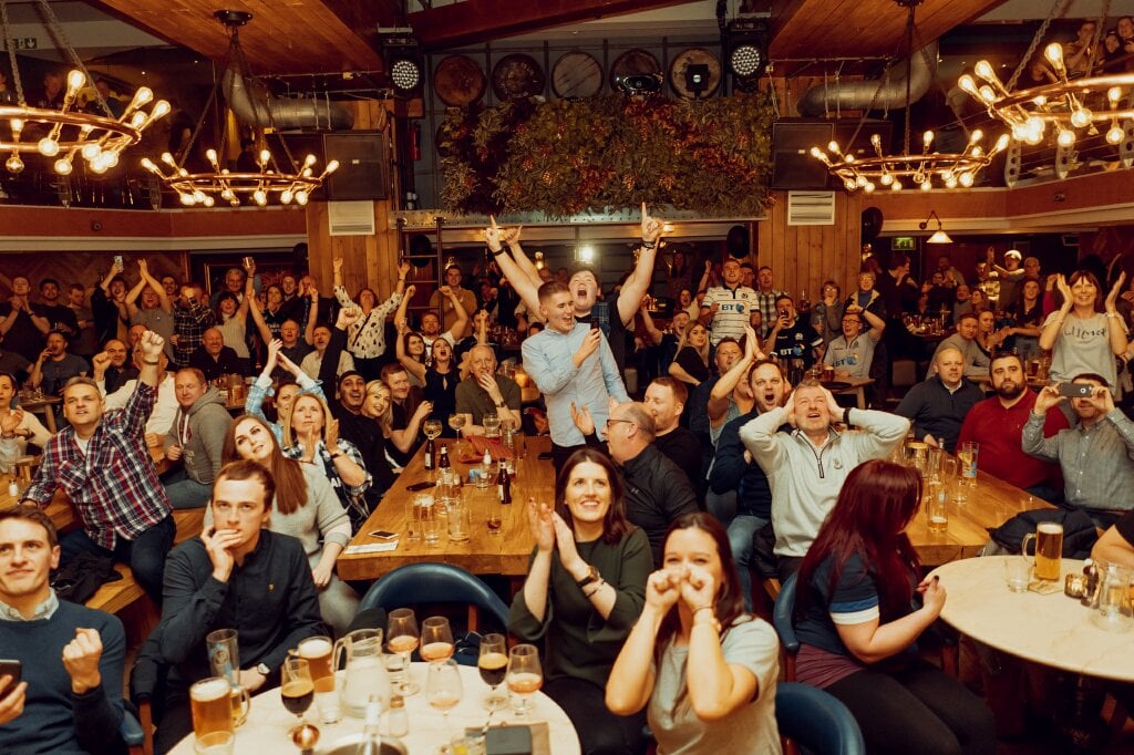 Room of people cheering happily at rugby dining at Brewhemia