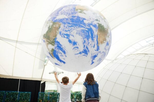Boy and girl in Dynamic Earth. Boy reaching up to touch large model of the earth as if holding it.