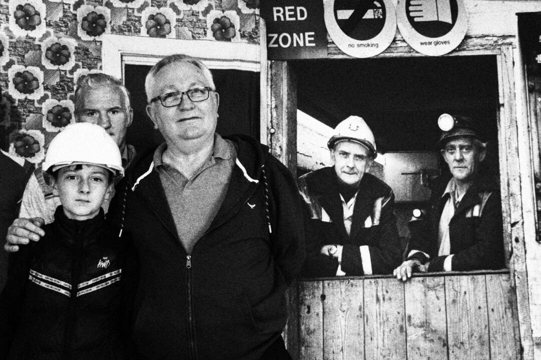 National Galleries Scotland, Peter and Grandson Former miner, Peter McCutcheon from Fife, with his grandson, in front of a banner displaying a Milton Rogovin photograph from 1982