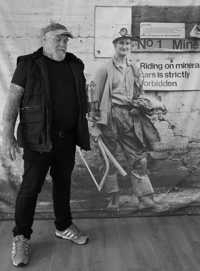 National Galleries Scotland, Donald Lamp Floor Former miner, Donald Fulton from Muirkirk, East Ayrshire, with his lamp, in front of a banner displaying a Milton Rogovin photograph from 1982