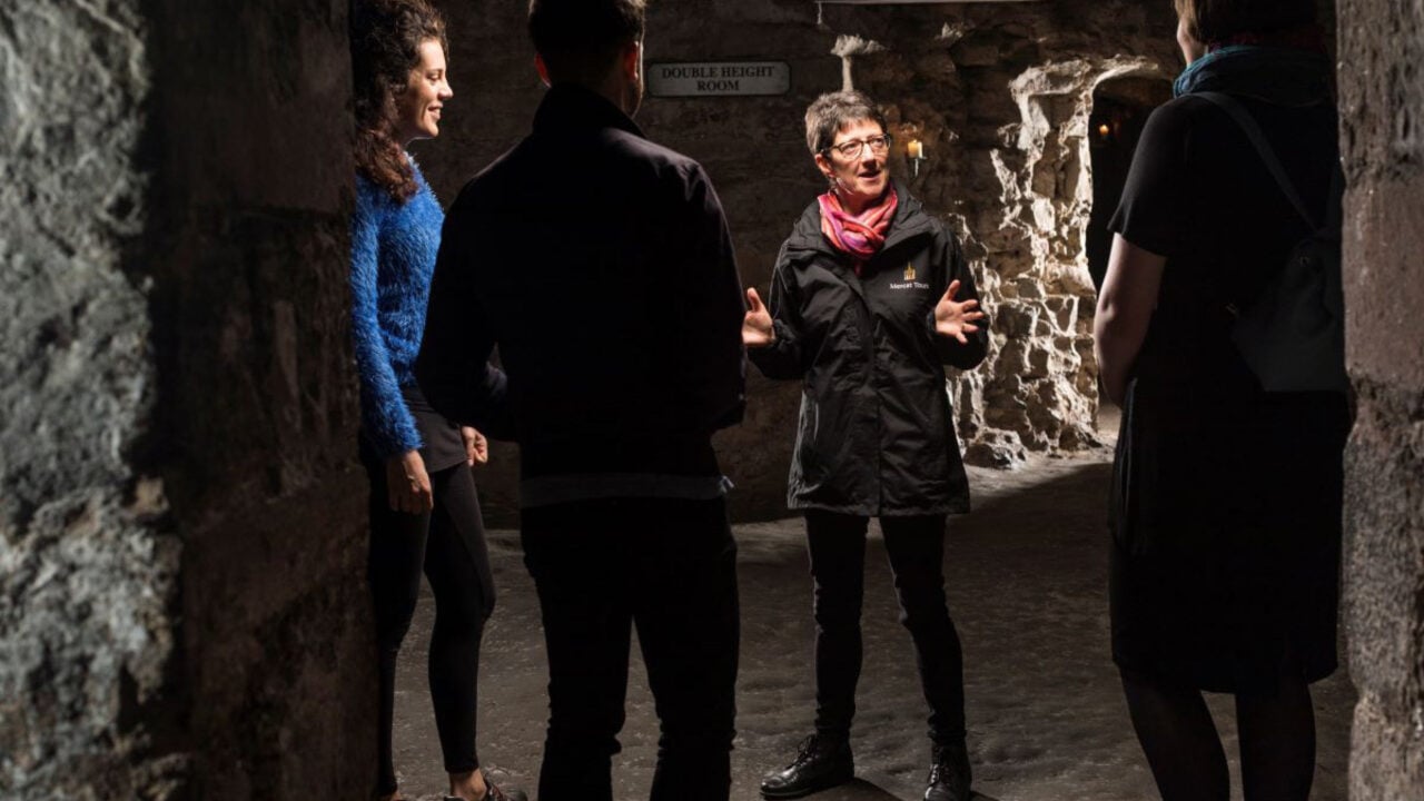 Mercat Tours Tour Guide in the Edinburgh Underground vaults with two tourists.