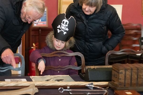 Kid dressed at pirate looking at book with grandparents at Trinity House