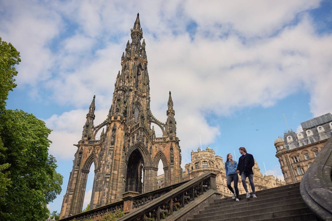 Young couple walking down stairs in Princes Street Gardens next to Scott Monument