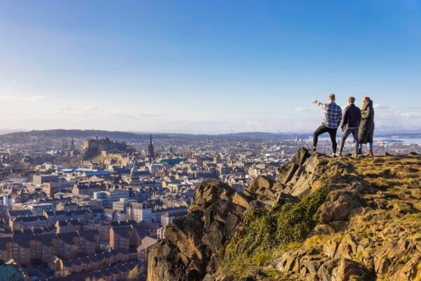 3 friends standing on Salisbury Crags looking to Edinburgh city view below.