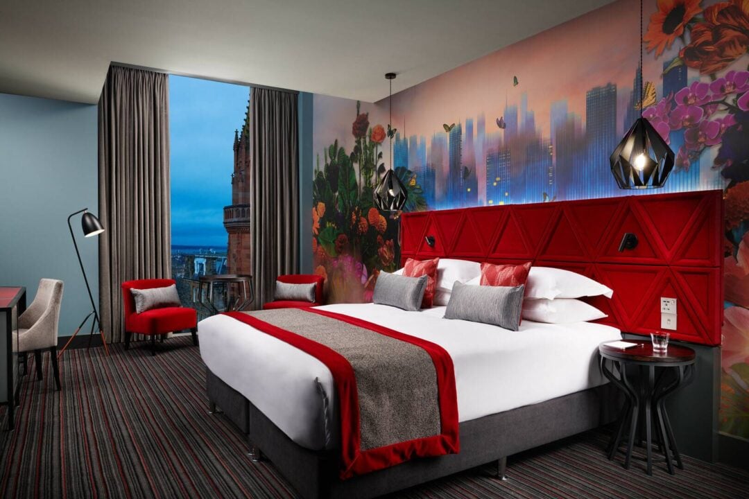 Stylish bedroom with large bed and cusions, attractive wall paper and city view