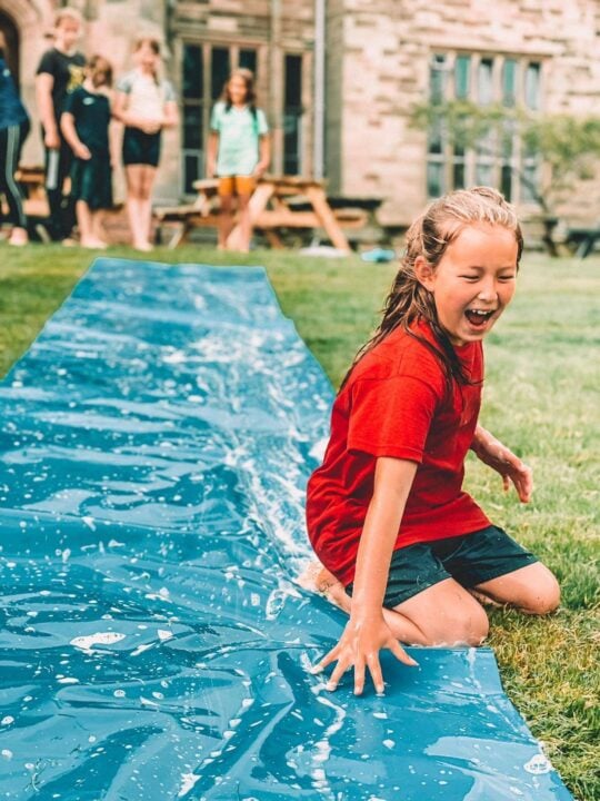 Picture of girl at previous summer camp on a slip and slide water slide. ,© The Wild Outdoors