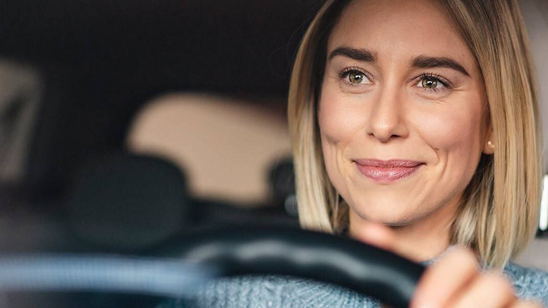 A smiling woman driving a rental car,© Avis Car Hire