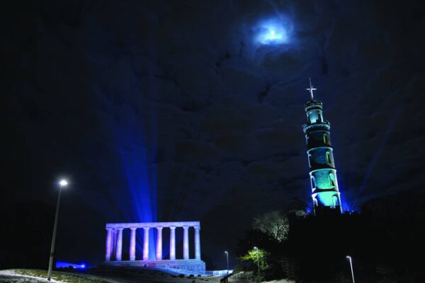 Nelson Monument lit up with blue and purple lights on Calton Hill.