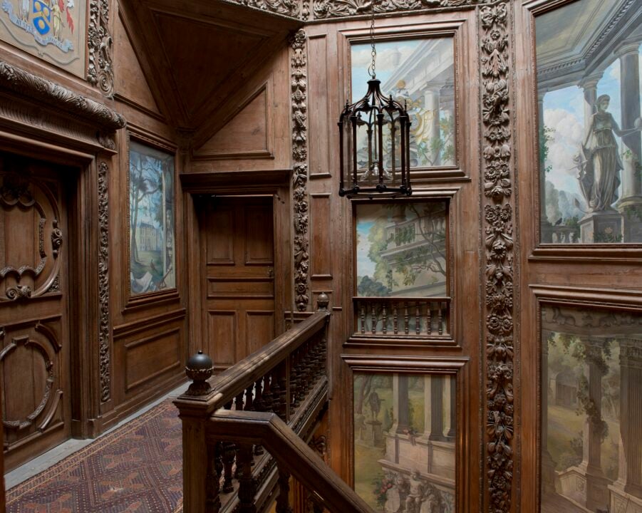 Wooden upper stair case filled with paintings.