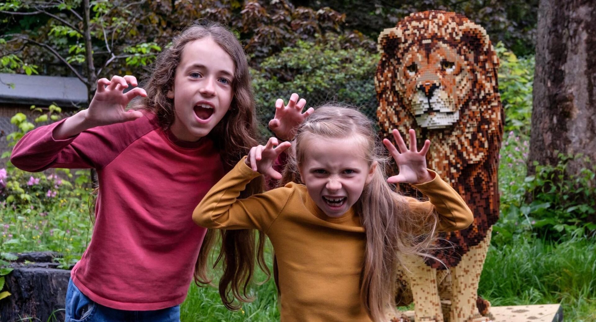 Two girls standing next to Lion made out of bricks