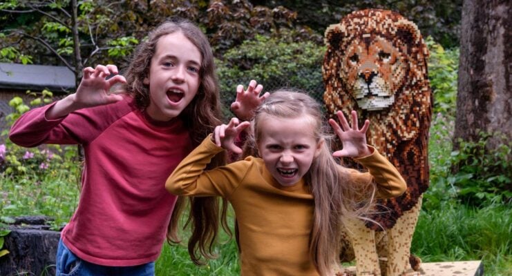 Two girls standing next to Lion made out of bricks