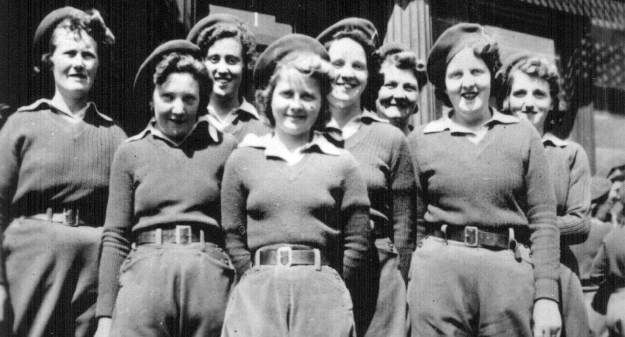 A black and white photograph of a group of women lumber jills in trousers, jumpers and hats, from 1942