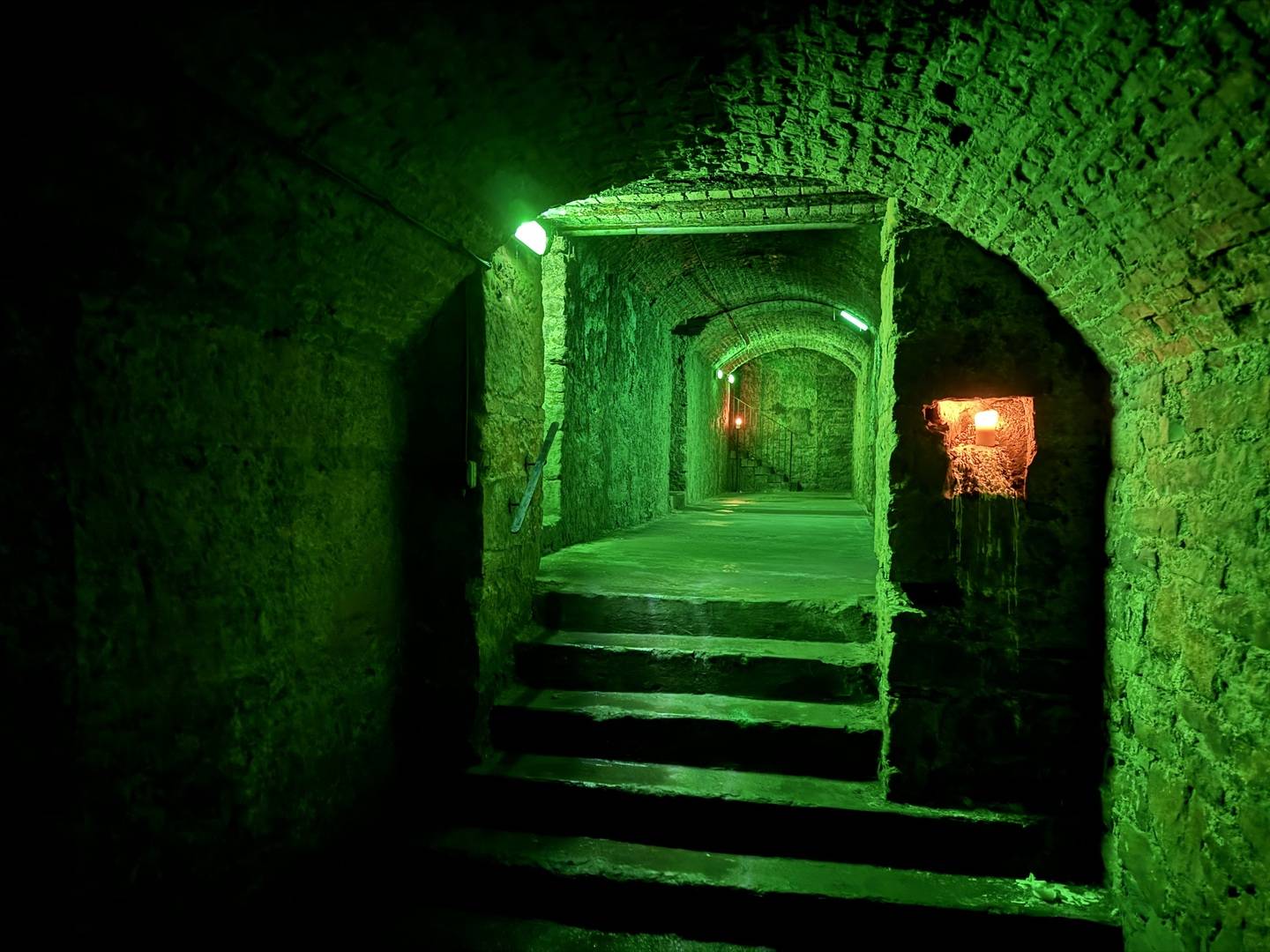 A corridor in the Niddry Street Vaults below Edinburgh South bridge illuminated by green emergency lights. ,© Auld Reekie Tours