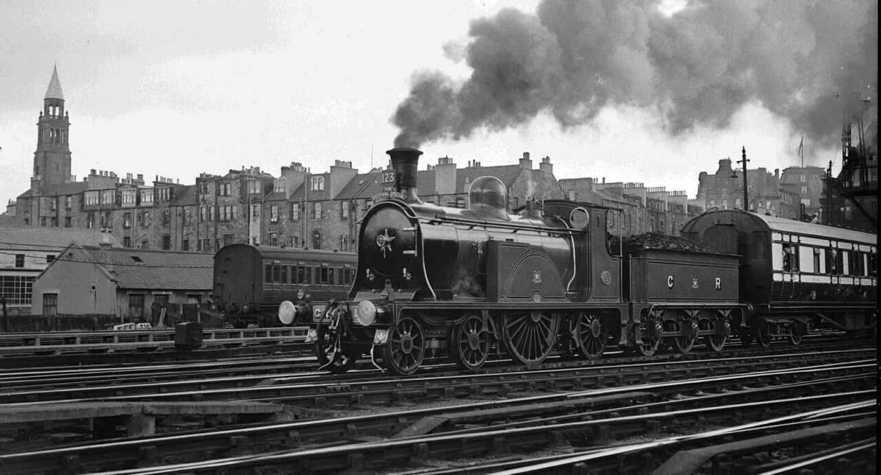 Steam train coming into station with Edinburgh buildings in background