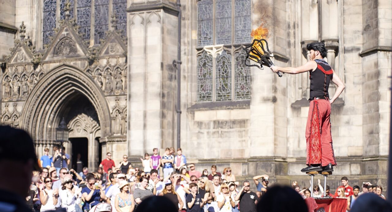 Fire juggler on stilts with crowd watching street performing ta Edinburgh Festival