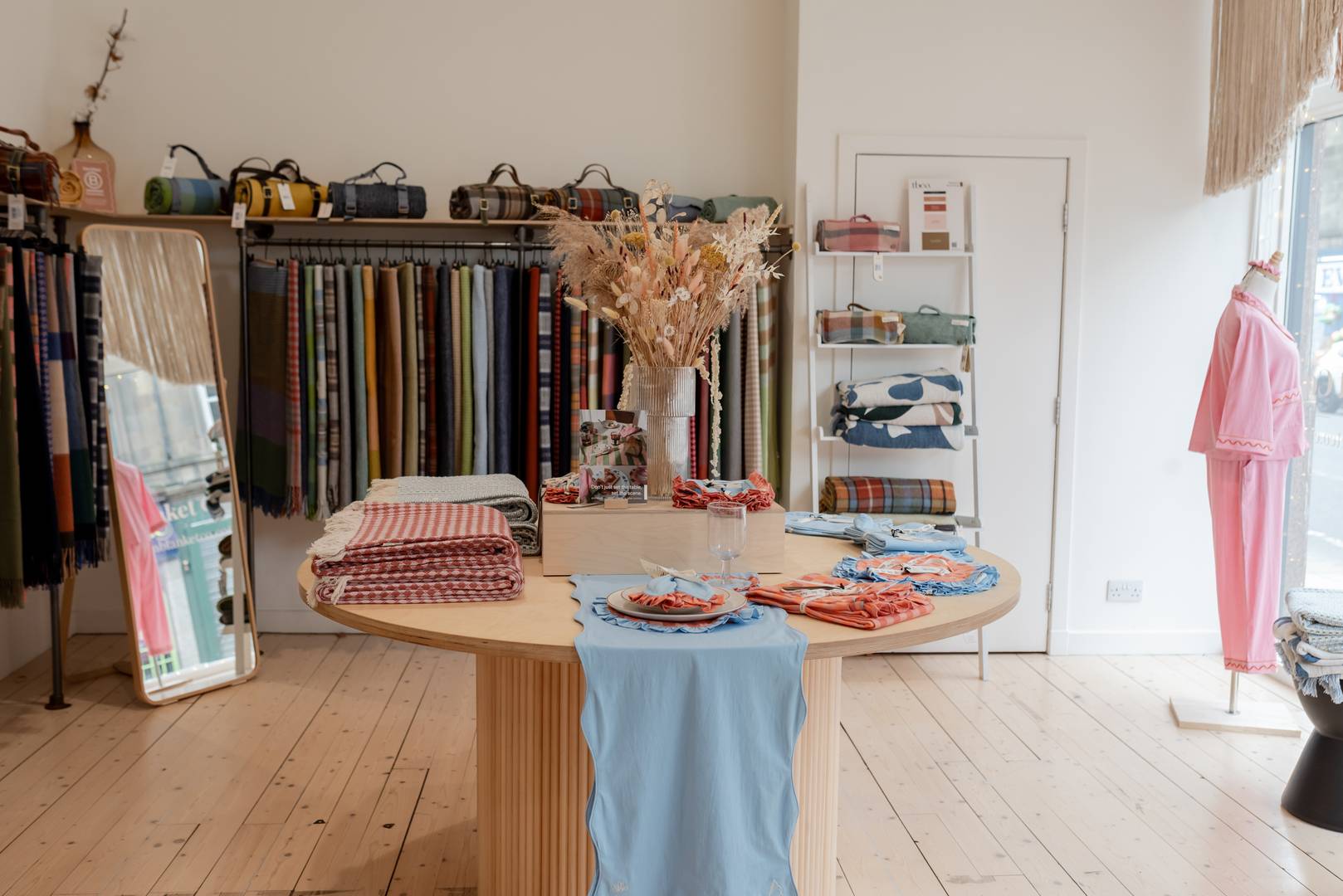 TBCo home wear section, featuring a variation of blankets alongside tableware set up on a circular wooden table.