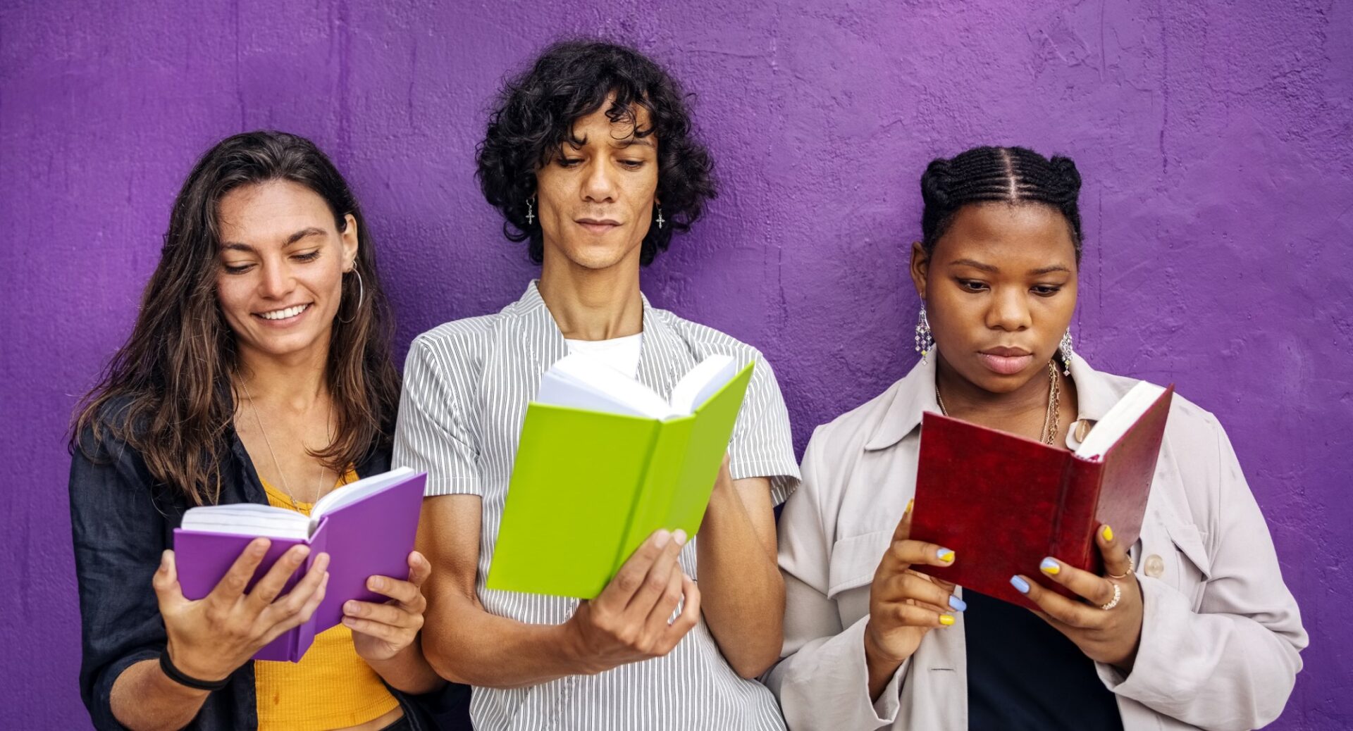 A young man and two young women standing against a lavender wall, each reading a book with a colourful but blank cover