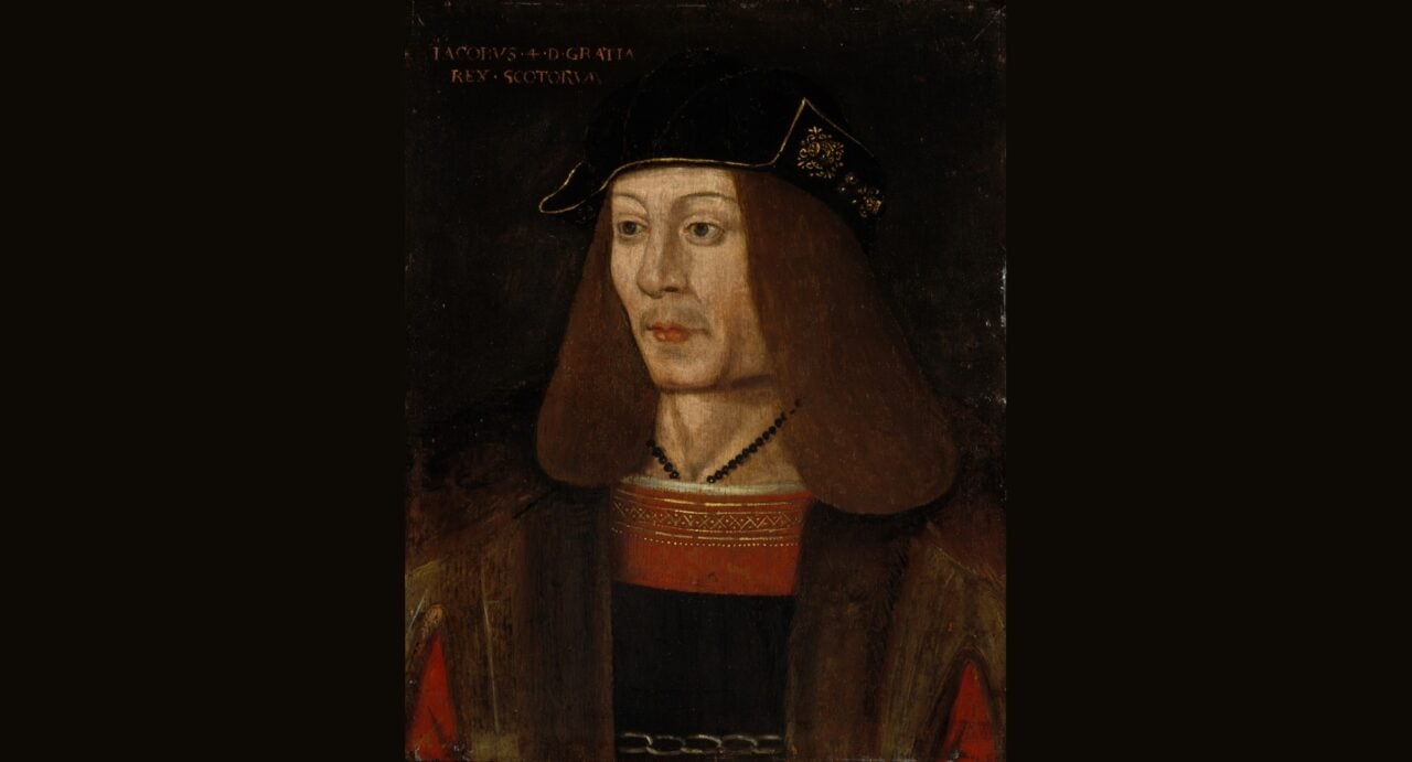 King James IV wearing a heavy brown coat and an orange and gold tunic, with a black necklace and a black and gold cap